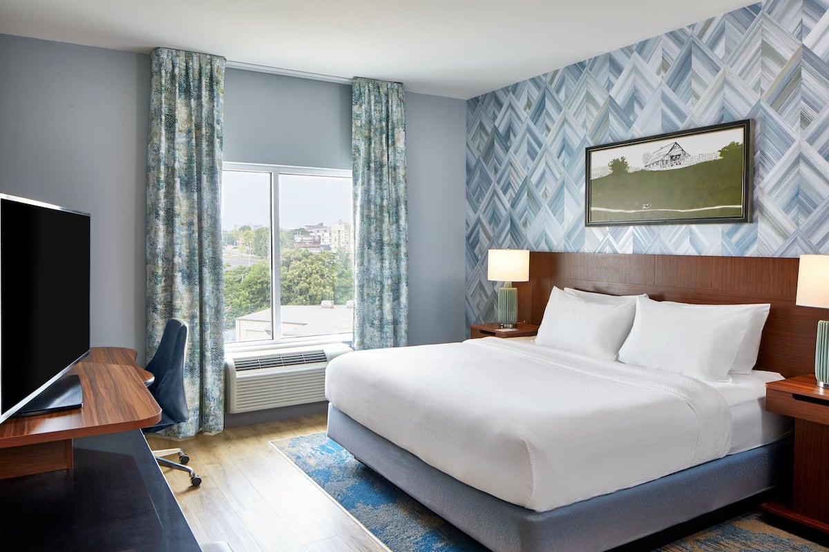 Habitación de hotel con una cama grande, un escritorio, un televisor y una ventana con cortinas.