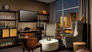 A modern living room with a city view, featuring a leather armchair, a round coffee table, and a striped armchair.