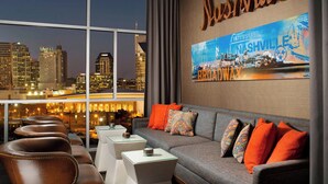 A modern hotel room with a large window offering a city view, a comfortable sofa with colorful cushions, and a wall-mounted sign reading "Nashville".