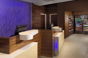 Zona de recepción con mostrador de madera, quiosco digital y minibar.