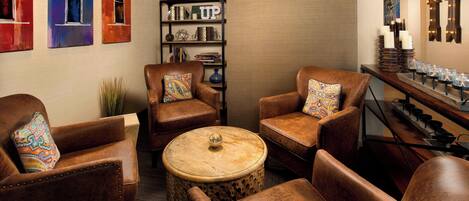 A cozy lounge area with leather armchairs, a round wooden table, and a bookshelf with various items.