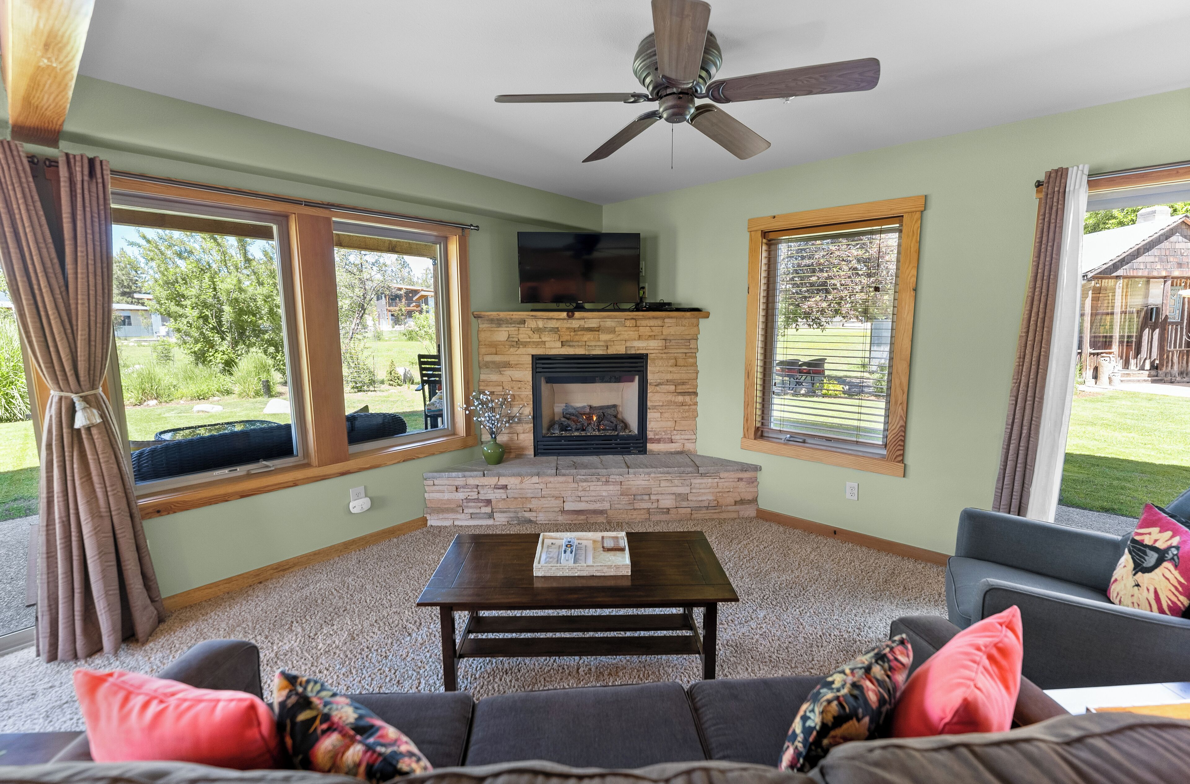 A living room with a fireplace, large windows, and a ceiling fan.