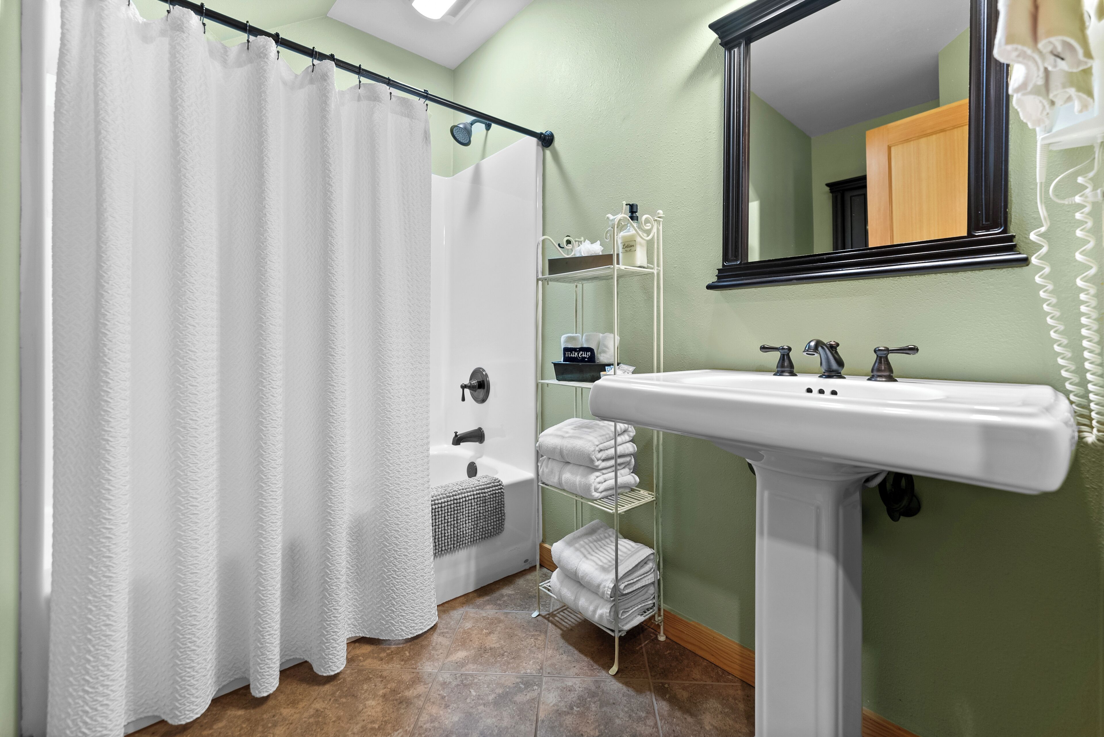 Un bagno con tenda da doccia, lavandino, specchio e porta asciugamani.