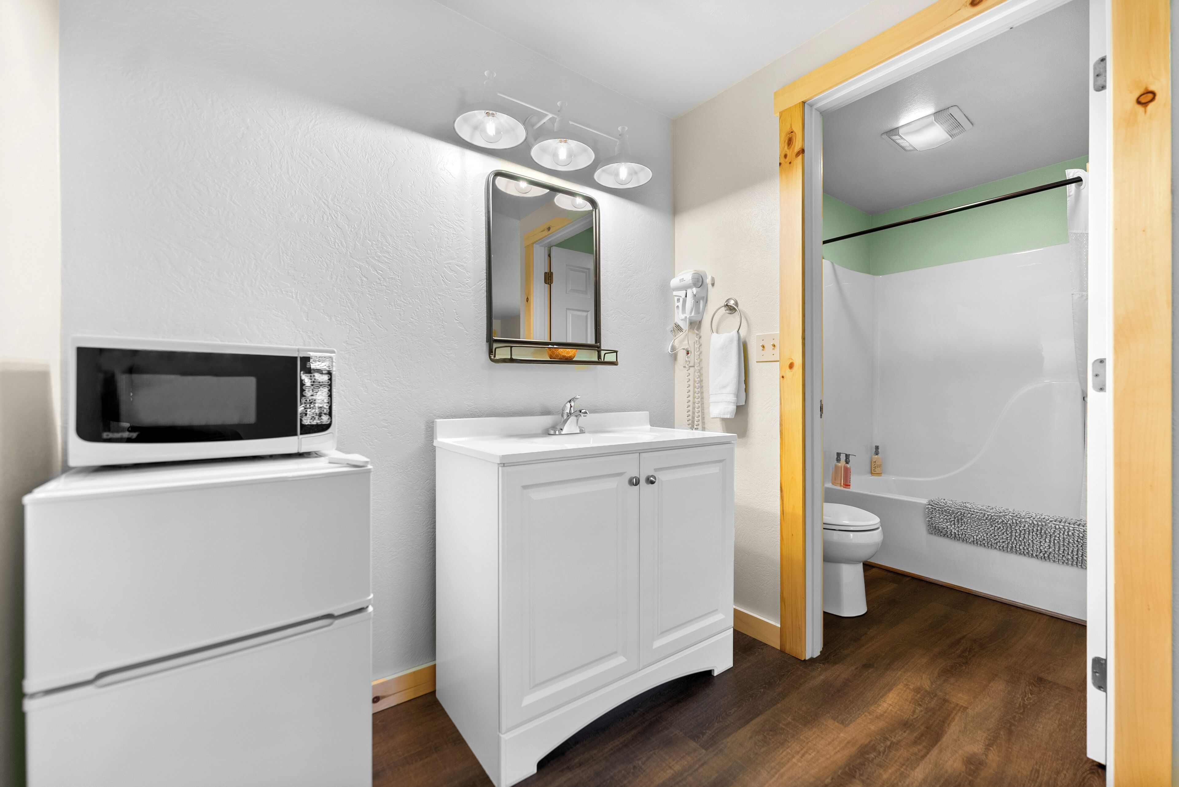 A bathroom with a white sink, a mirror, a toilet, a shower, and a microwave.