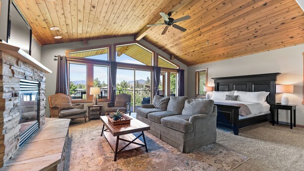 A spacious living room with a fireplace, a large sofa, a coffee table, and a bed with a headboard. - Mt Gardner Inn (Winthrop)