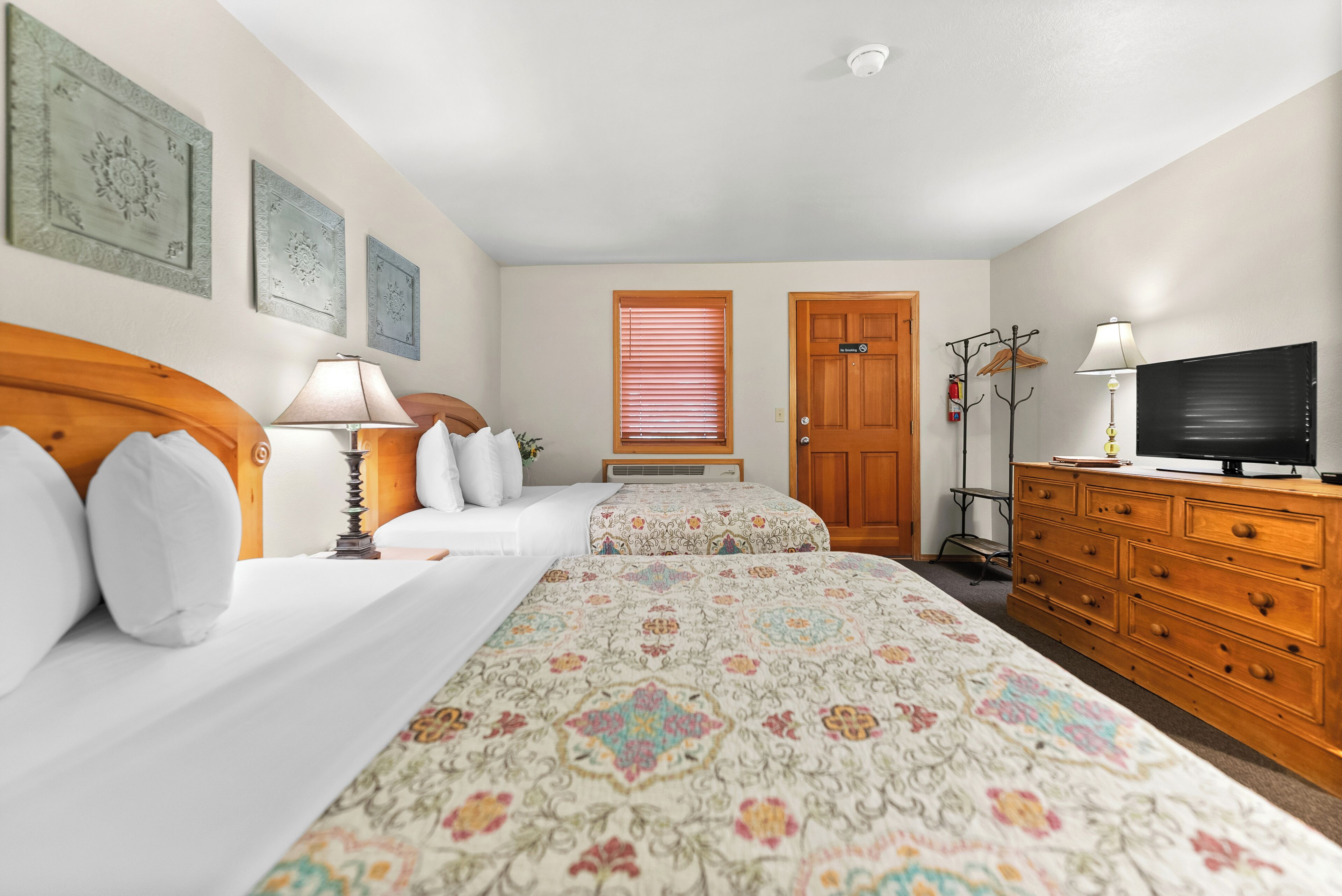 A hotel room with a bed, a dresser, a television, and a window with blinds.