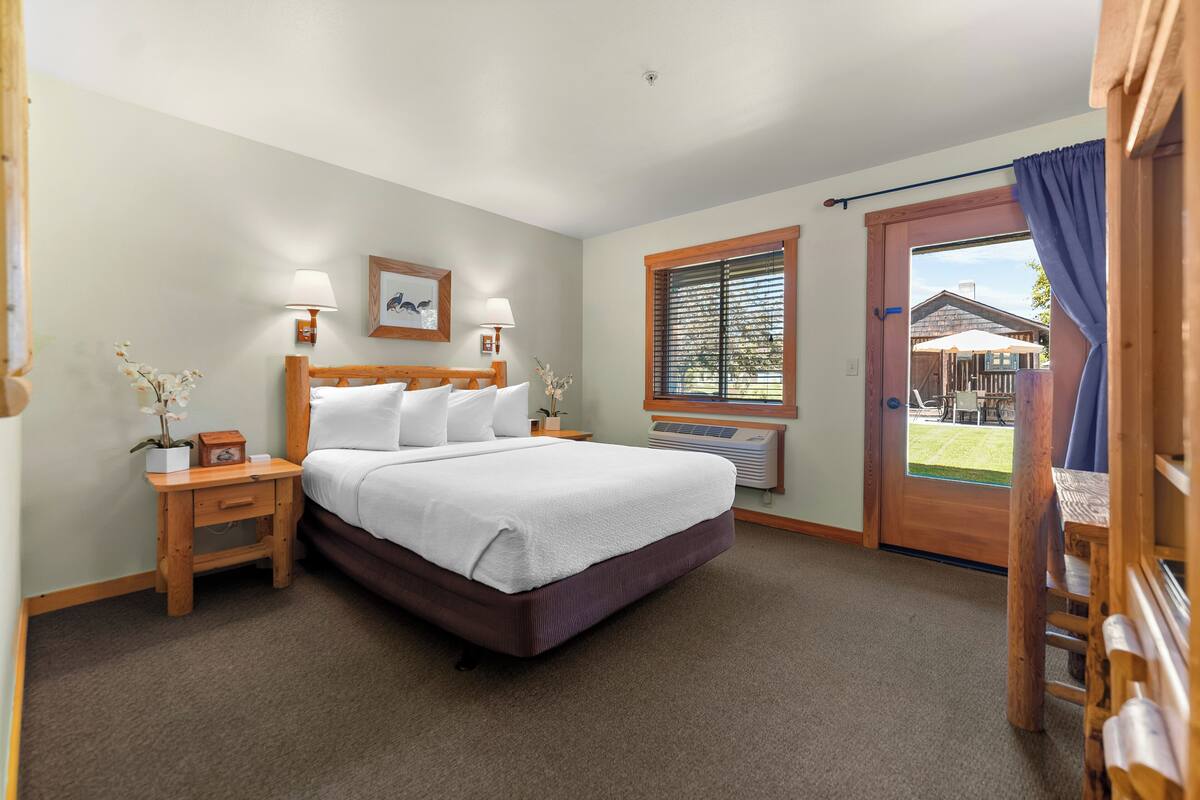 Um quarto com cama, mesas de cabeceira, janela com persianas e porta que dá para o exterior.