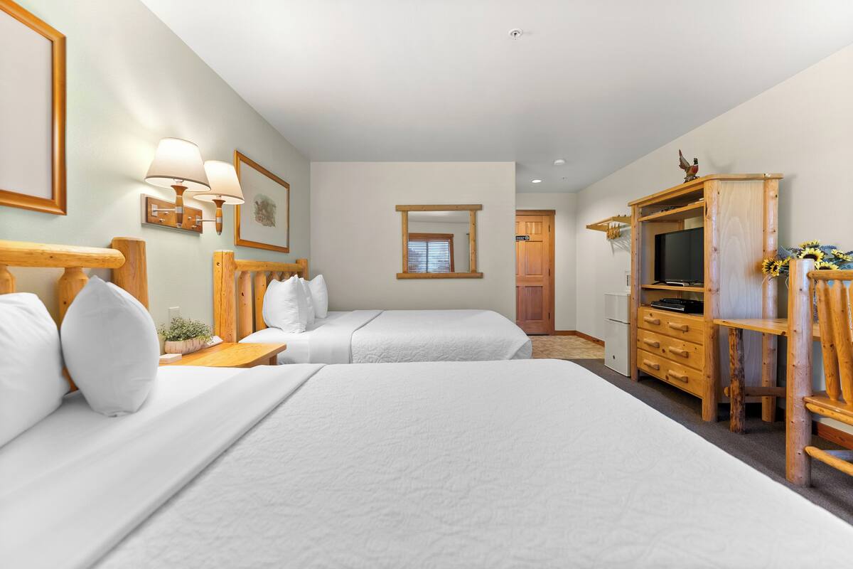 Quarto de hotel com duas camas, um aparador de madeira, uma televisão e um espelho.