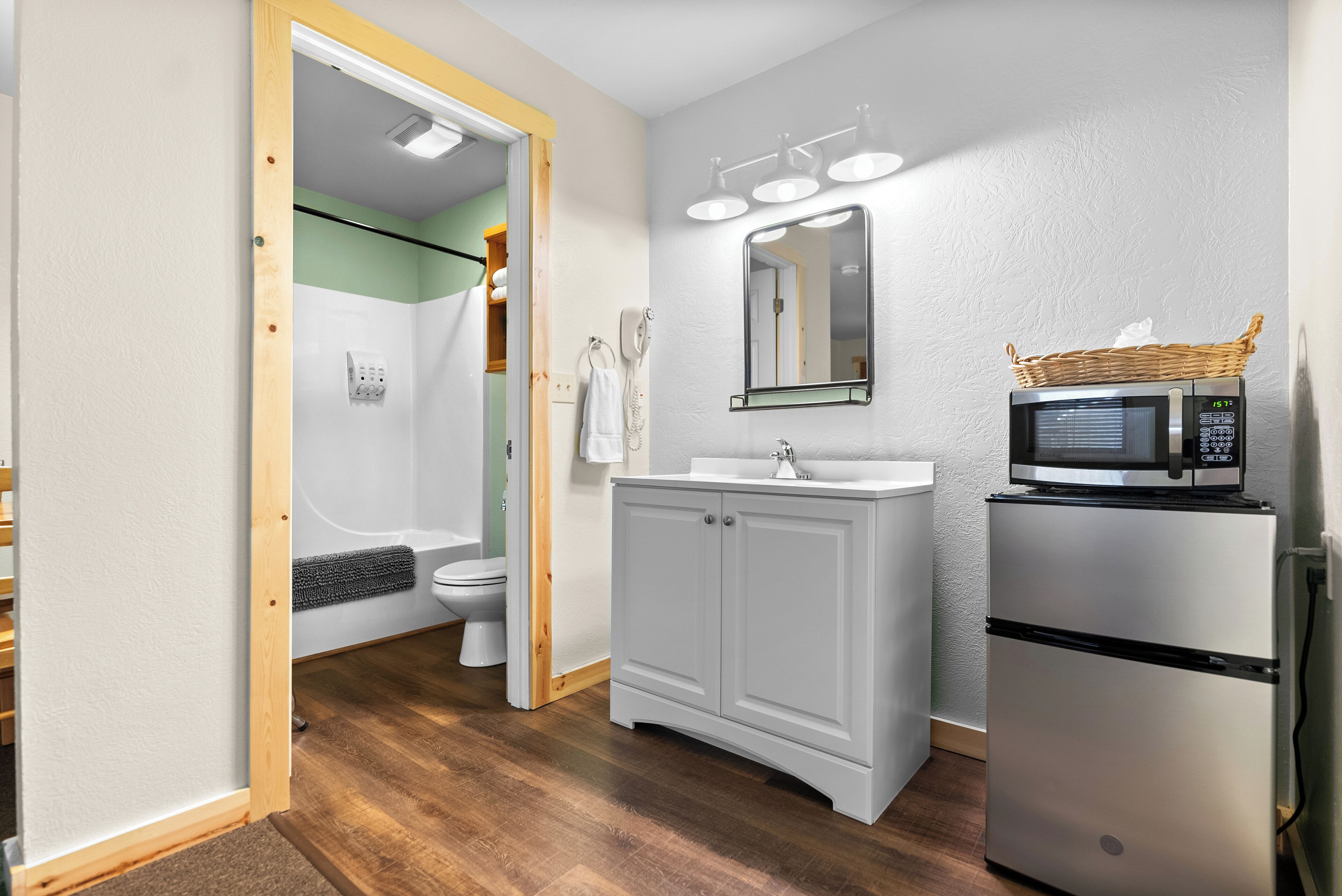 A bathroom with a shower, toilet, vanity, and a microwave on a small refrigerator.