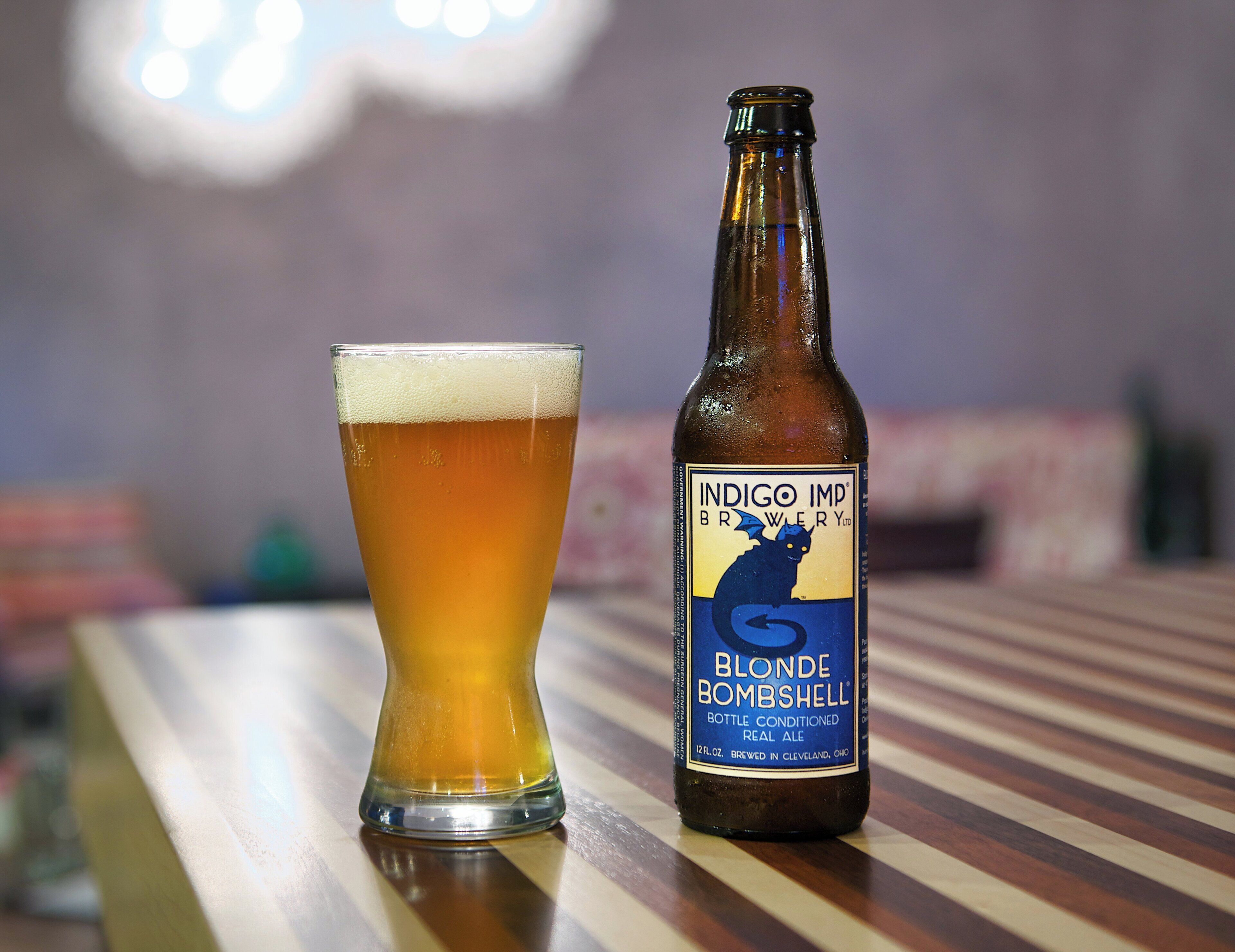 A bottle of Blonde Bombshell beer next to a glass on a wooden surface.