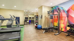 Een fitnessruimte met loopbanden, een bank, een rek voor squatten en kleurrijke fitnessballen.