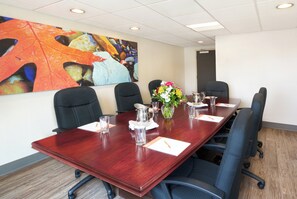 Une salle de conférence avec une longue table, des chaises noires, un vase rempli de fleurs et un tableau accroché au mur.