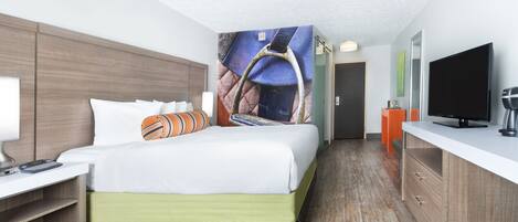 A hotel room with a bed, a desk with a lamp, a television, and a coffee maker.