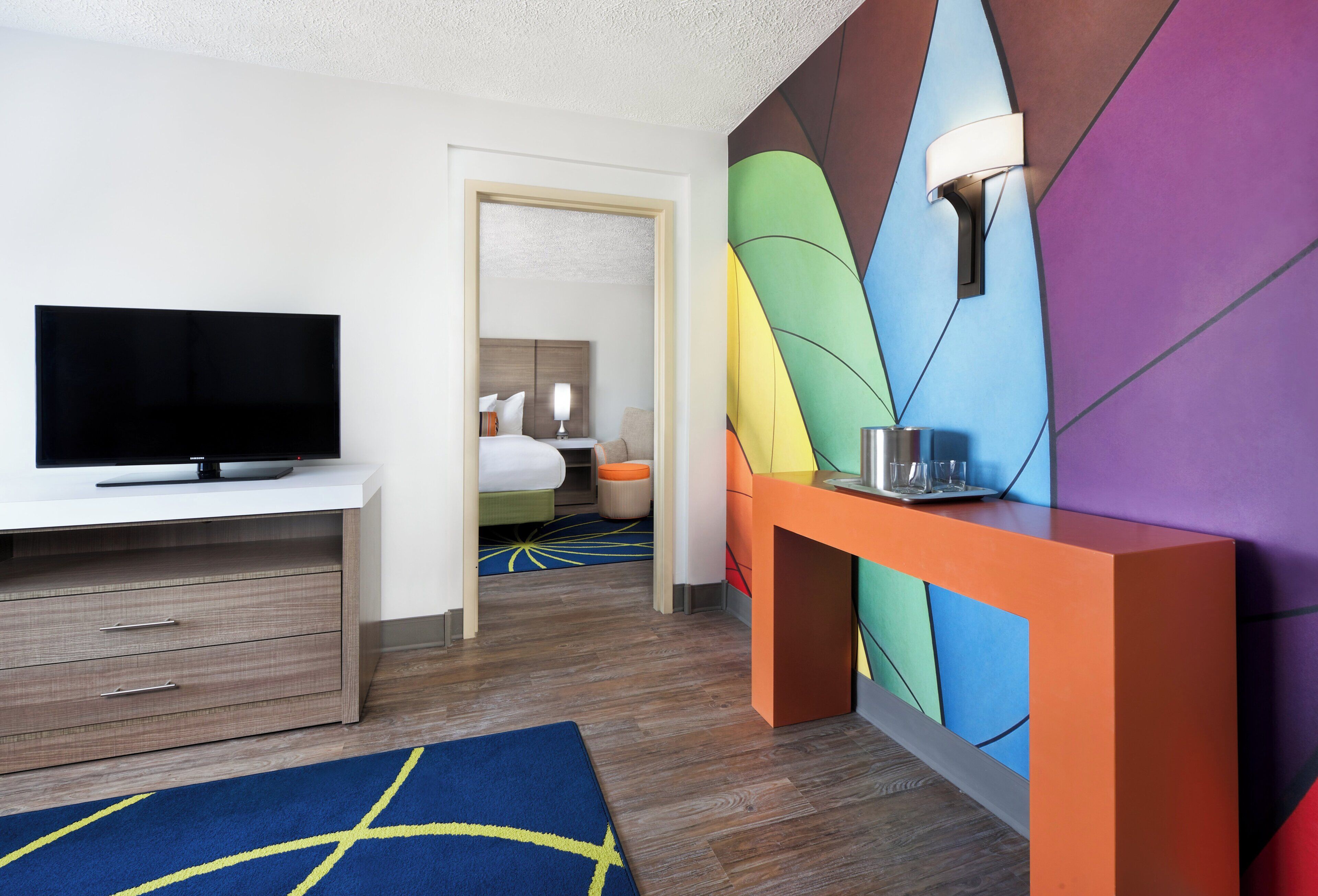 Una habitación de hotel con televisión, escritorio, pared de colores y cama.