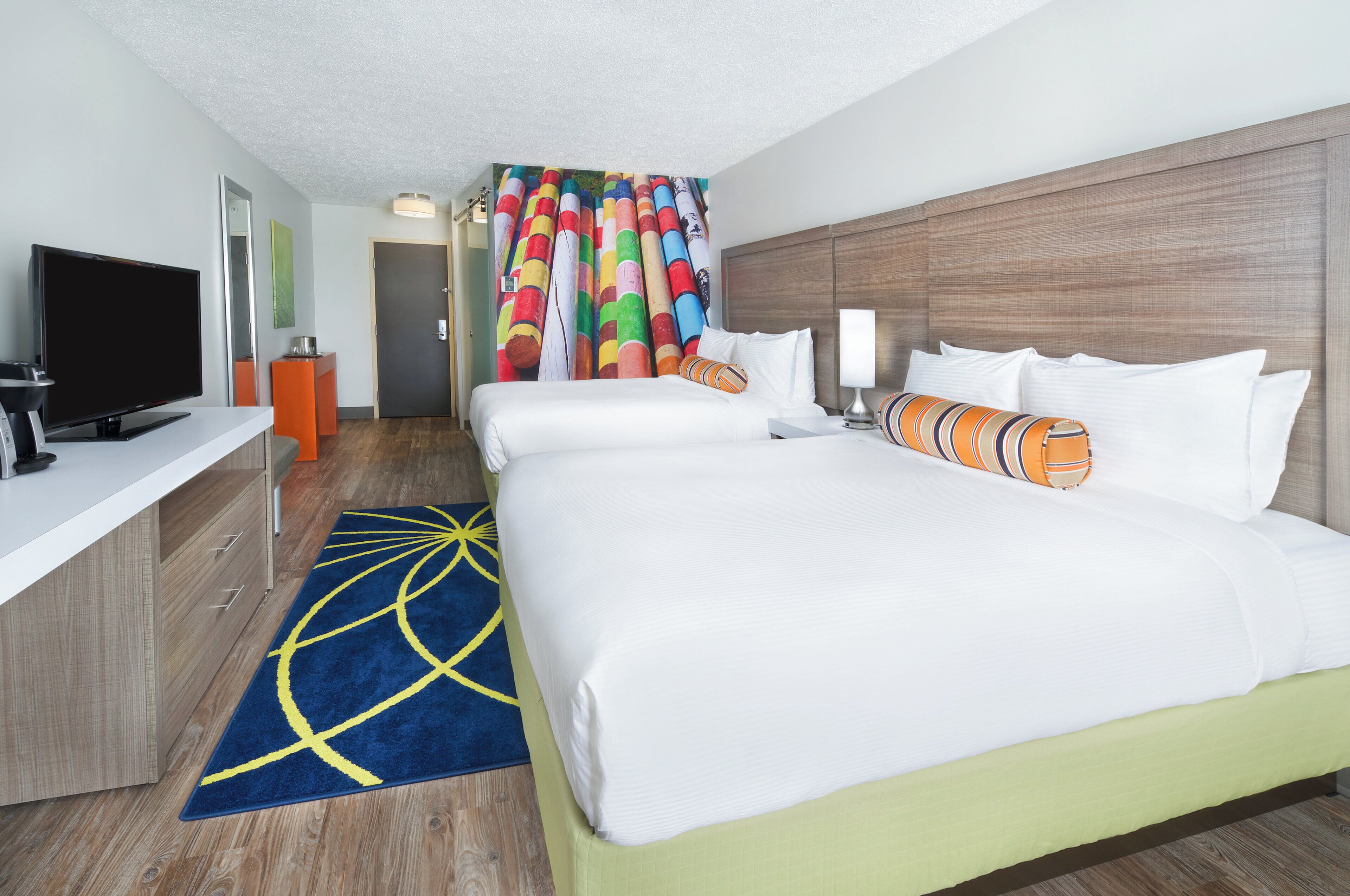 A hotel room with a large bed, a TV, a desk, and a colorful curtain.
