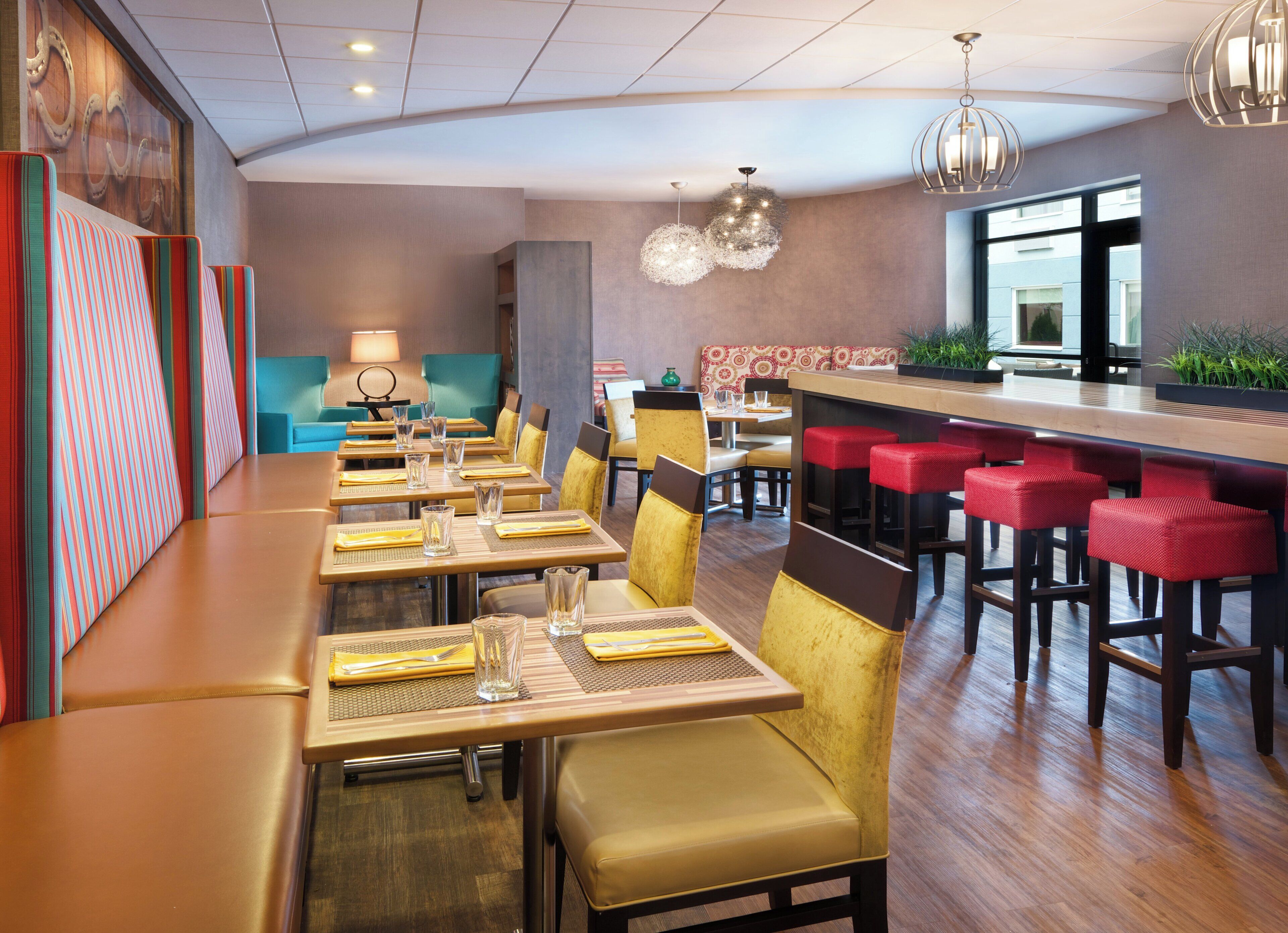 Un restaurante con cabinas, mesas altas y una zona de bar, con vista al exterior.