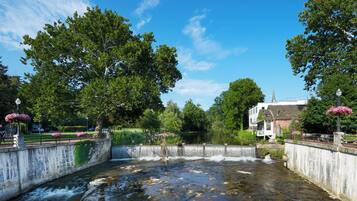Un río atraviesa un parque con un puente, árboles y un edificio con aguja.