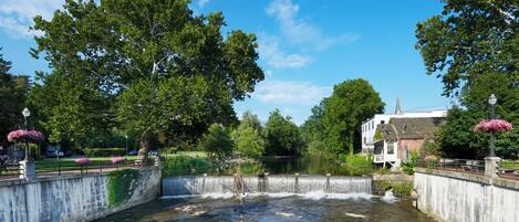 Ein Fluss fließt durch einen Park mit einer Brücke, Bäumen und einem Gebäude mit einem Turm.