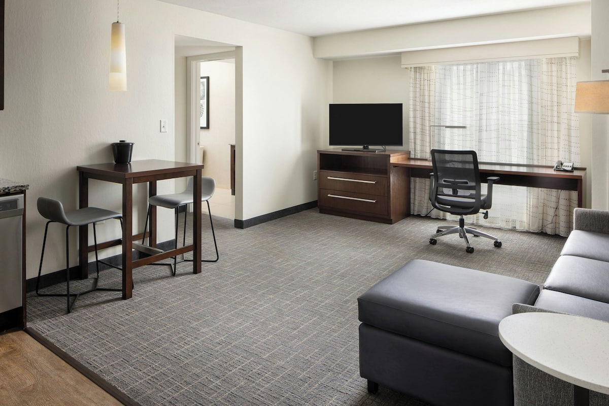 A hotel room with a desk, a television, a sofa, a chair, and a small table.