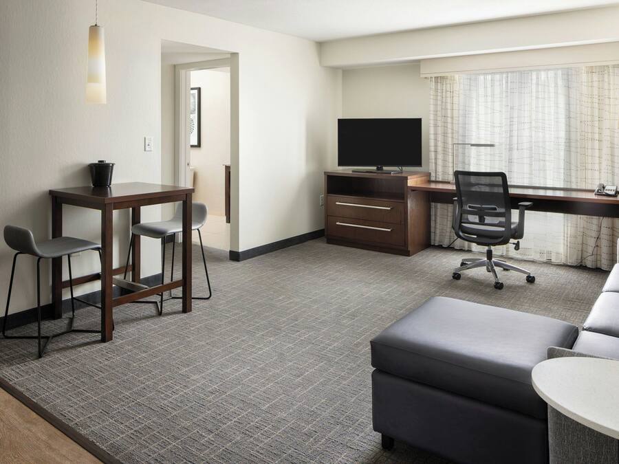 Una habitación de hotel con escritorio, televisor, sofá, sillón y una pequeña mesa.