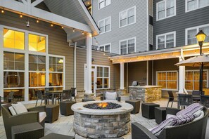 An outdoor patio with stone fire pit, wicker furniture, and string lights.
