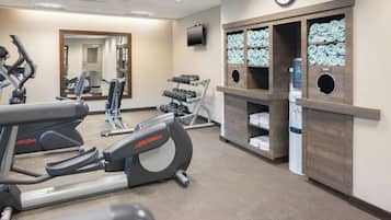 Ett gym med konditionsmaskiner, en spegel, en tv och prydligt staplade handdukar och vattenflaskor.