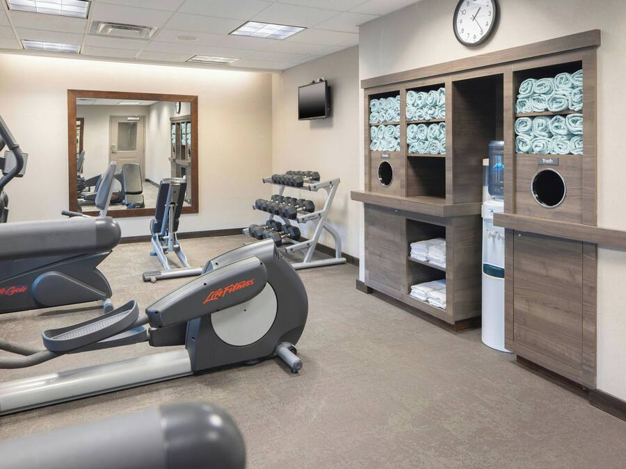 Ett gym med konditionsmaskiner, en spegel, en tv och prydligt staplade handdukar och vattenflaskor.