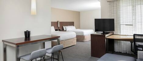 Una habitación de hotel con escritorio, dos camas, televisión y zona de estar.