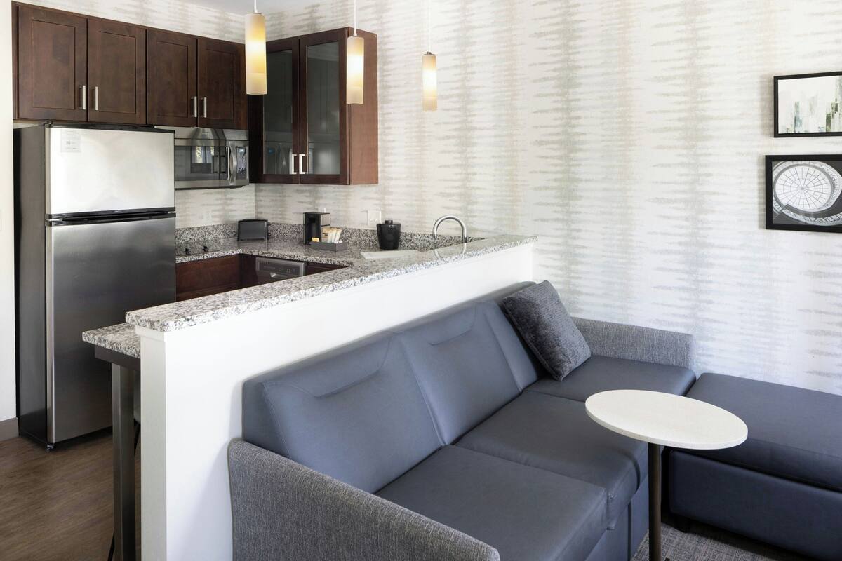 A modern kitchen with a built-in island, dark wooden cabinets, stainless steel appliances, and a gray sofa with a small table.