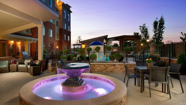 An outdoor patio area with a central water feature, seating arrangements, and a pool in the background. - Residence Inn Nashville SE/Murfreesboro (Murfreesboro)