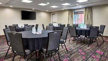 A conference room with round tables, chairs, a flat-screen TV, and a window with curtains.