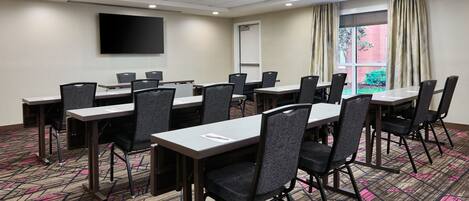 A conference room with multiple tables and chairs, a flat-screen TV, and a projector screen.