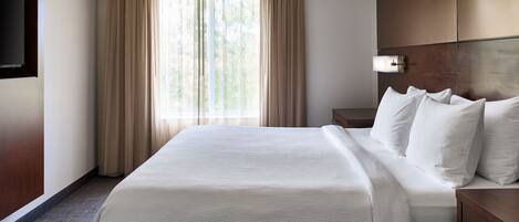 A hotel room with a large bed, a flat-screen TV mounted on the wall, a bedside table, and a window with curtains.