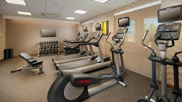 Un gimnasio con cintas de correr, elípticas y una banca.