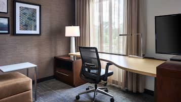 Habitación de hotel con escritorio, silla, lámpara, televisor y sofá.