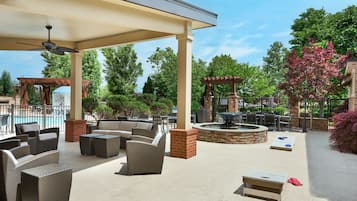 Een terras buiten met rieten meubilair, een vuurkorf van steen en een zwembad op de achtergrond.