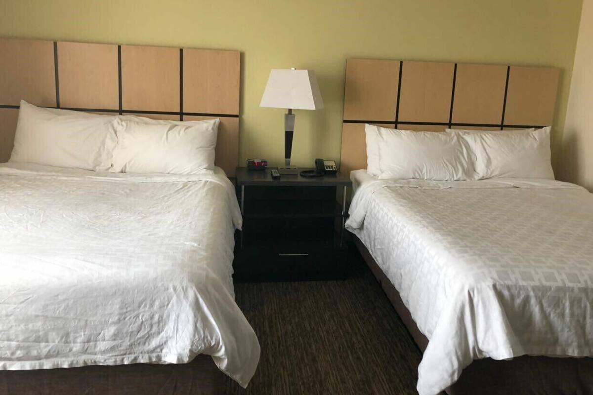 Ein Hotelzimmer mit zwei Betten, einem Nachttisch mit Lampe sowie einem kleinen Tisch mit Telefon und Fernbedienung.