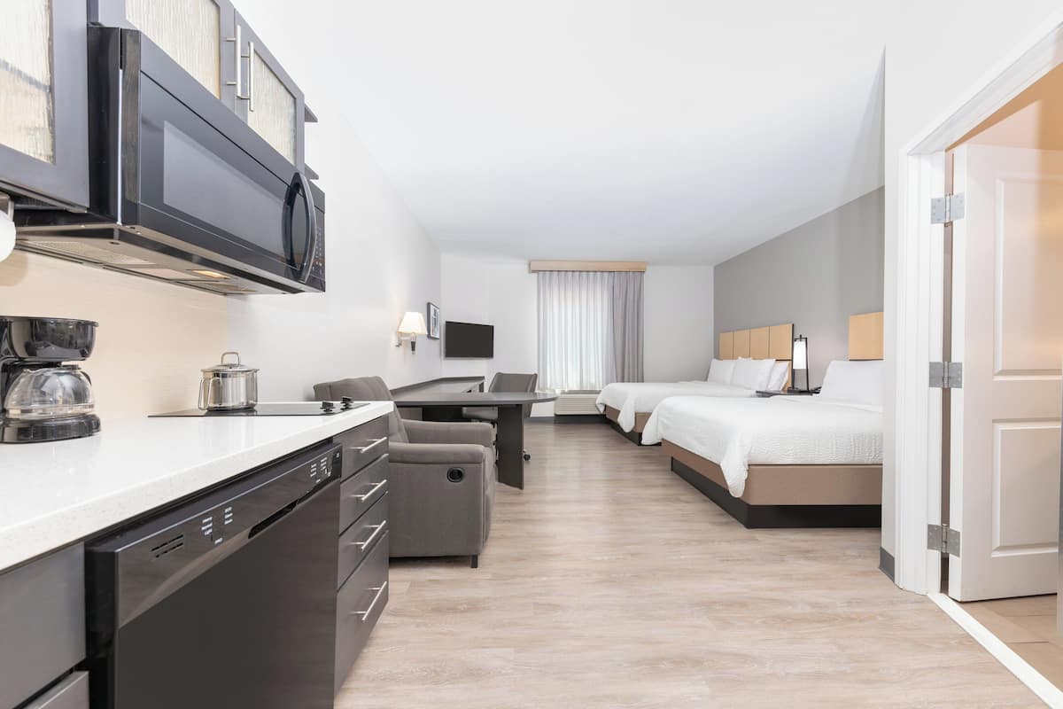 Ein modernes Hotelzimmer mit einer Küchenzeile, einem Bett, einem Schreibtisch und einer Sitzecke.