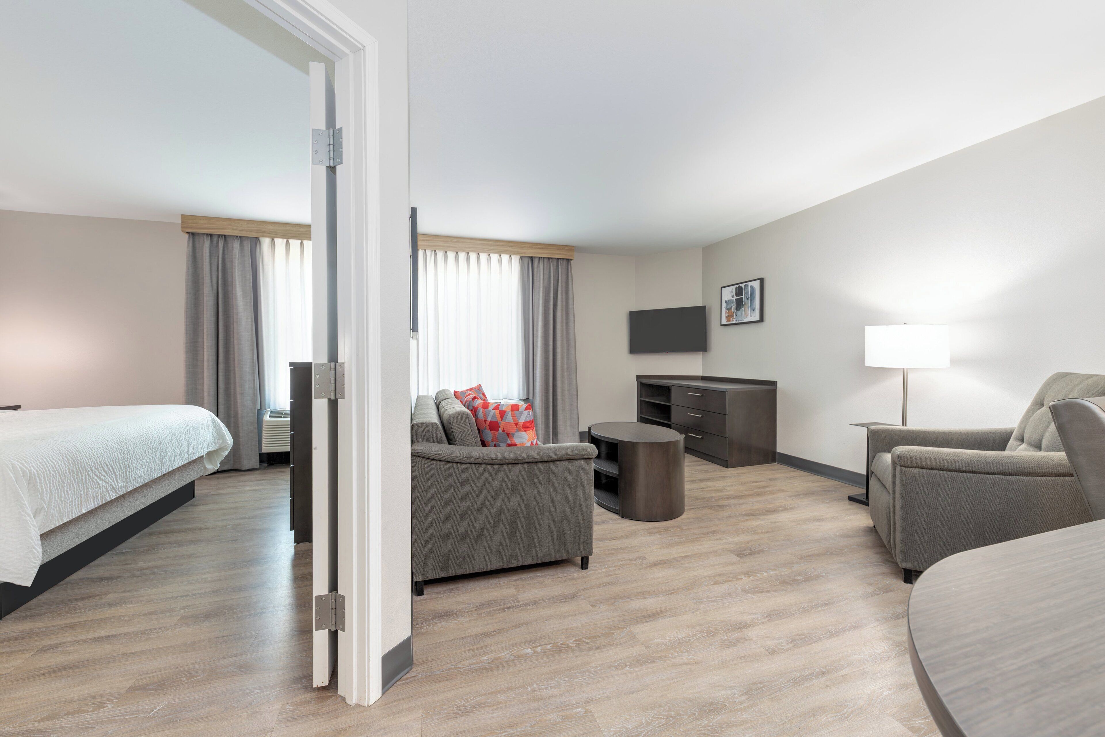 Et moderne hotelværelse med seng, to sofaer, fjernsyn, skrivebord og lampe.