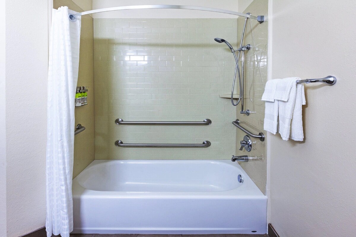 A bathroom with a bathtub, grab bars, a showerhead, and a towel rack.