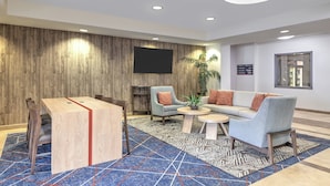 En moderne lobby med trævæg, et fladskærms-tv, en sofa, et sofabord og et spiseområde med stole.