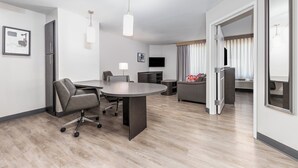 Et moderne hotelværelse med spiseplads, sofa, TV og et stort vindue med gardiner.