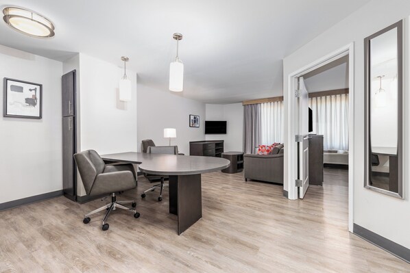 A modern hotel room with a dining area, a sofa, a TV, and a large window with curtains. - Candlewood Suites Midland SW by IHG (Midland)