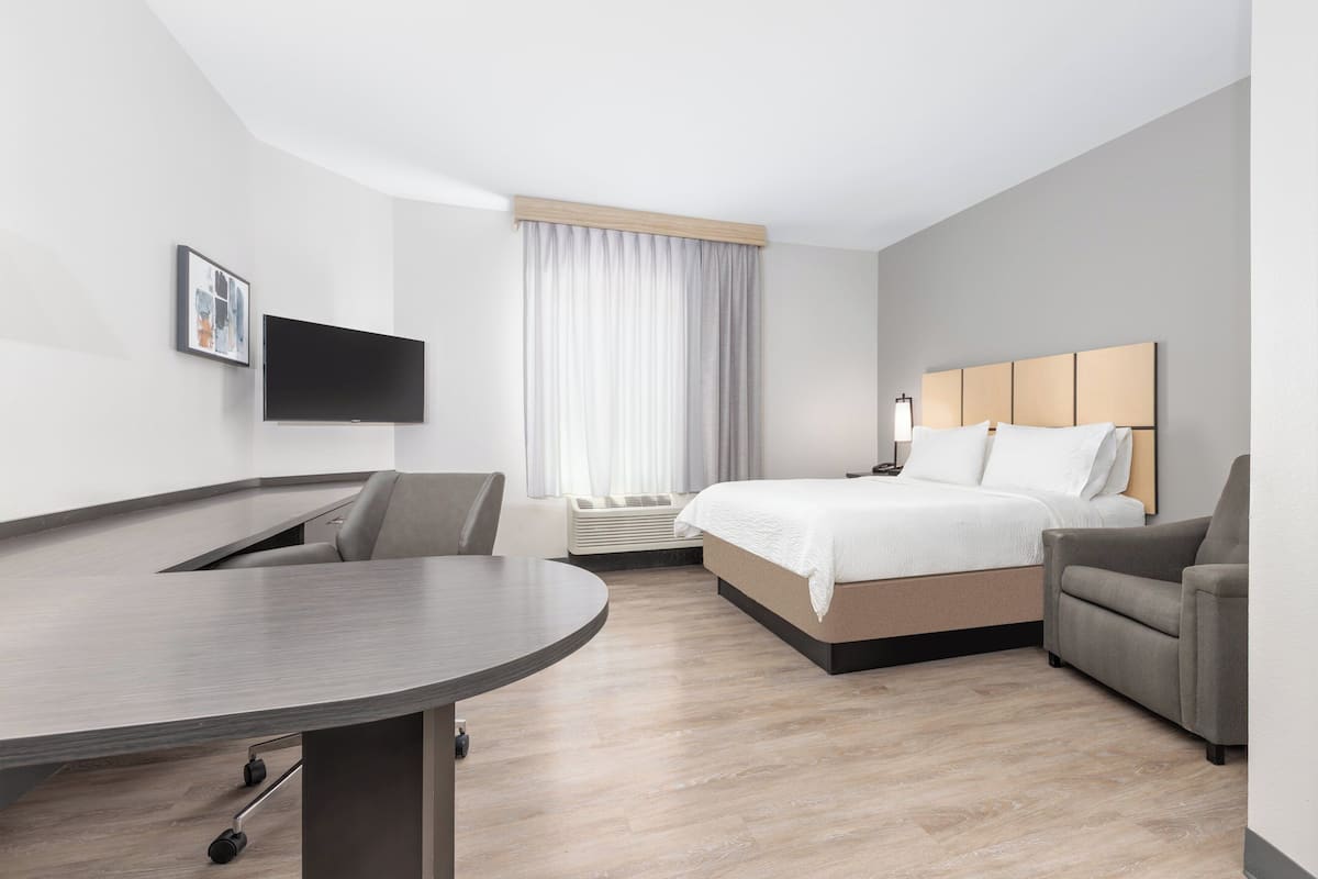 Ein modernes Hotelzimmer mit Bett, Schreibtisch, Stuhl, Flachbildfernseher und einem großen Fenster mit Vorhängen.