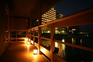A wooden deck with a railing overlooking a body of water and a cityscape at night.