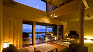 En moderne stue med et stort skydedørsvindue, der fører ud til en balkon, en sofa, et sofabord og et fjernsyn.