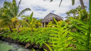Un resort tropical con un edificio de techo de paja, rodeado de exuberante vegetación y una masa de agua tranquila.
