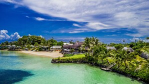Un resort tropical con playa, aguas cristalinas y exuberante vegetación.