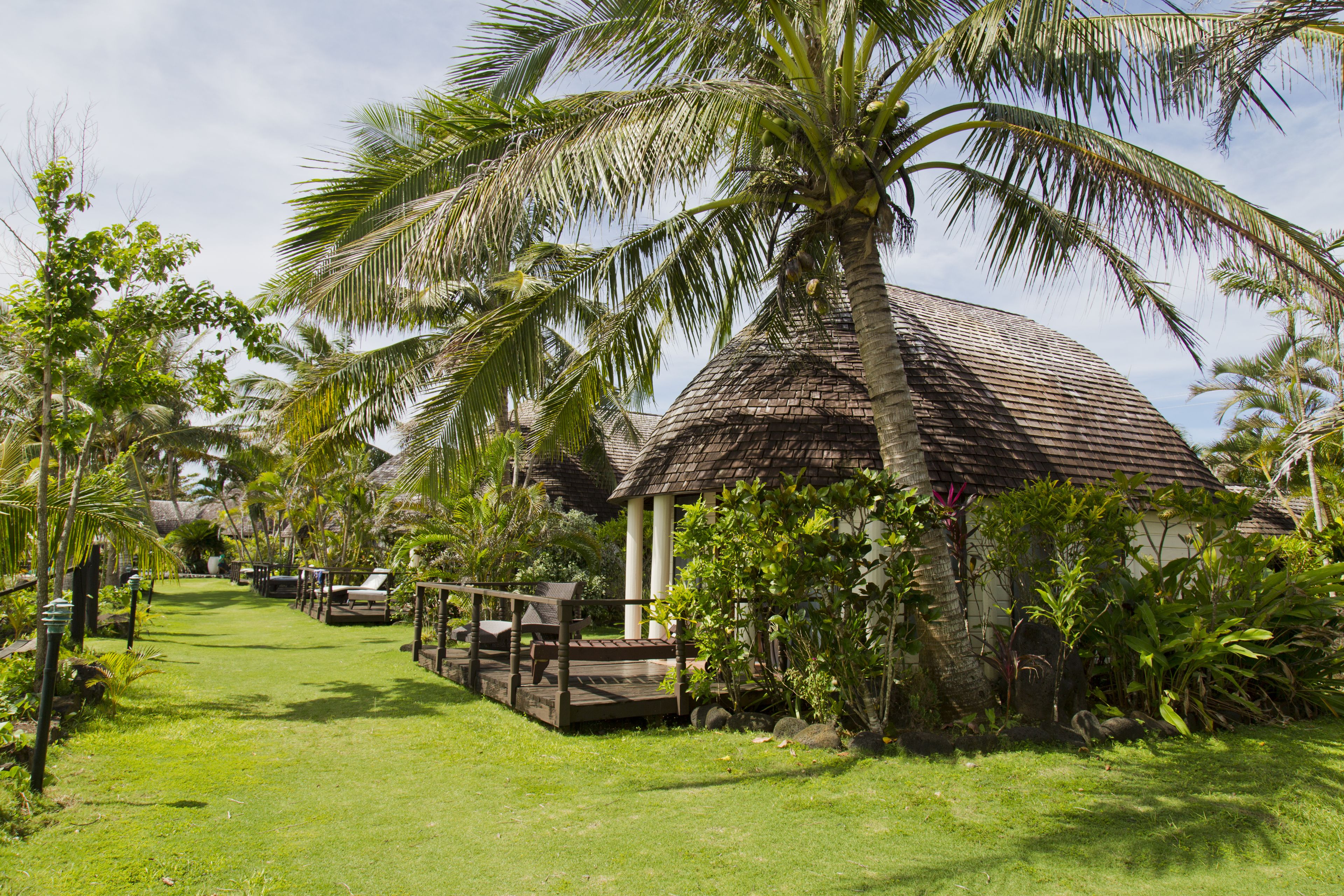 A tropical resort with a thatched-roof hut, a wooden deck, and lush greenery.