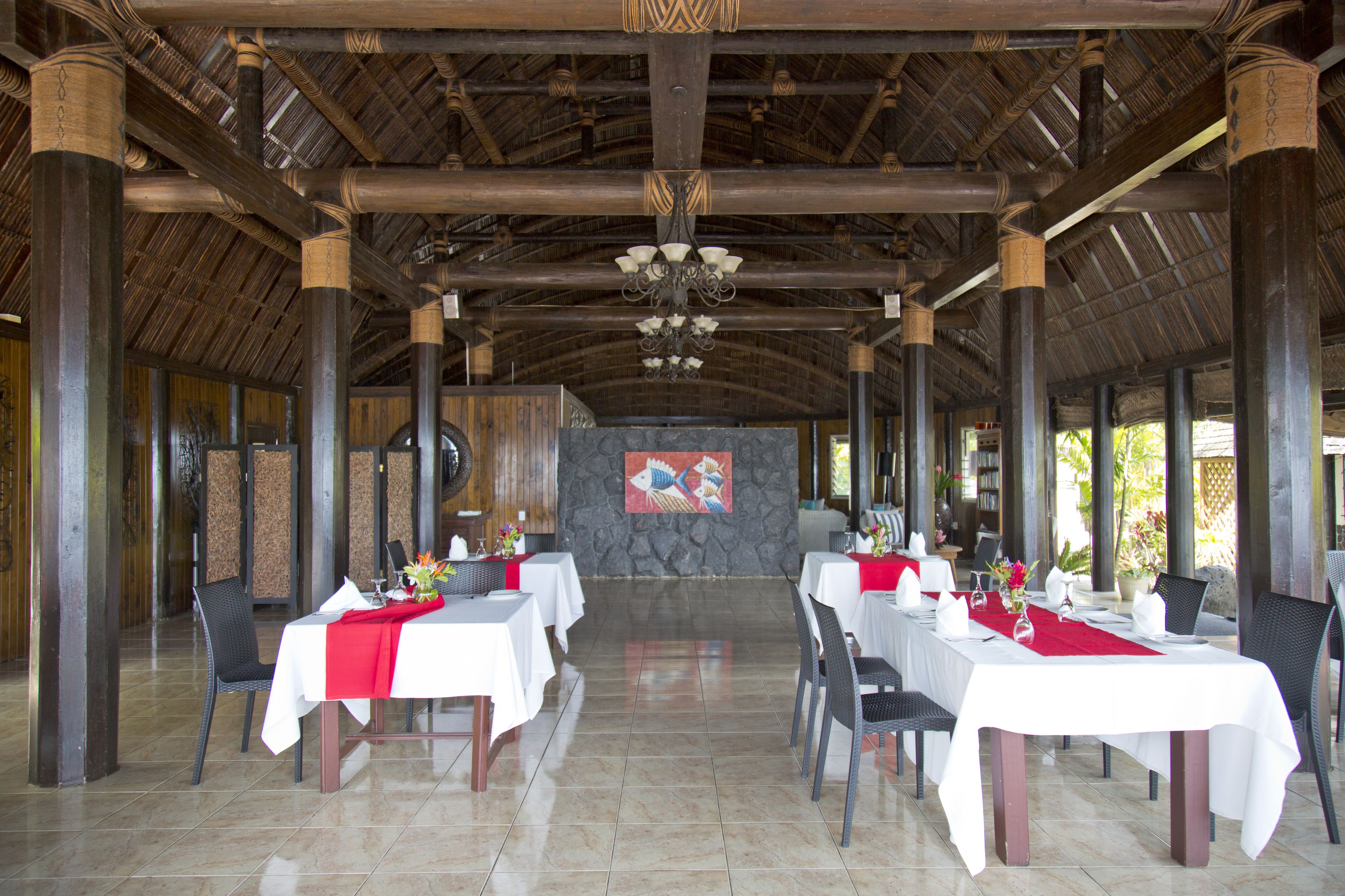 A spacious indoor dining area with high ceilings and wooden beams, featuring tables set for dining with white tablecloths and red runners.